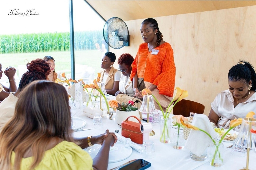 Dr. Angel Mbome standing and sharing at the intimate luncheon table surrounded by women at the Glowing with Intentionality event